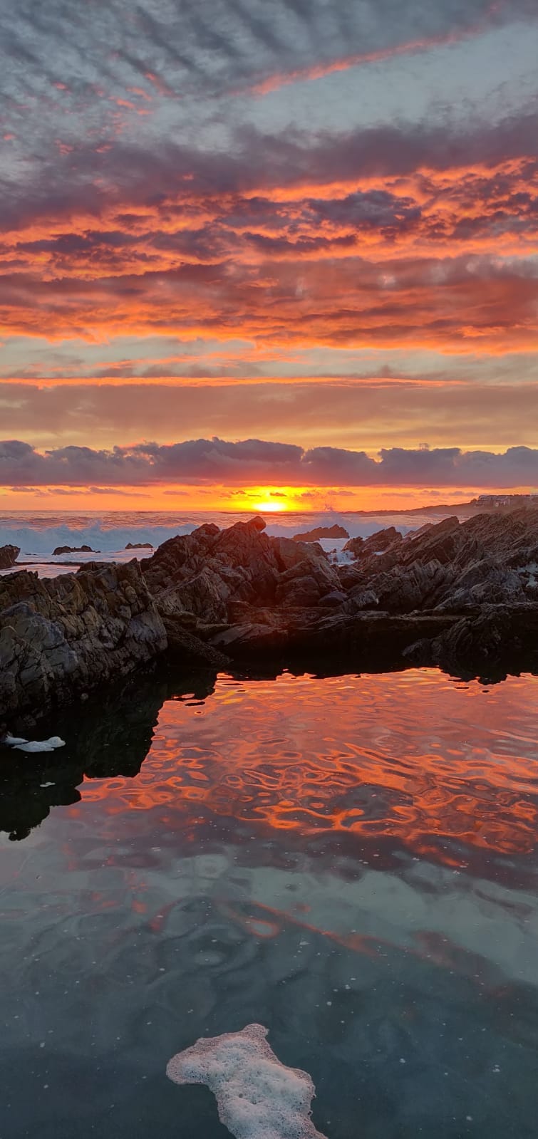 Davies tidal pool at Onrus reflecting an orange sunset, dark rocks ringing the still water